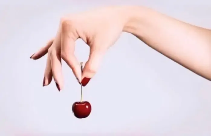 Hand holding a cherry with red nails.
