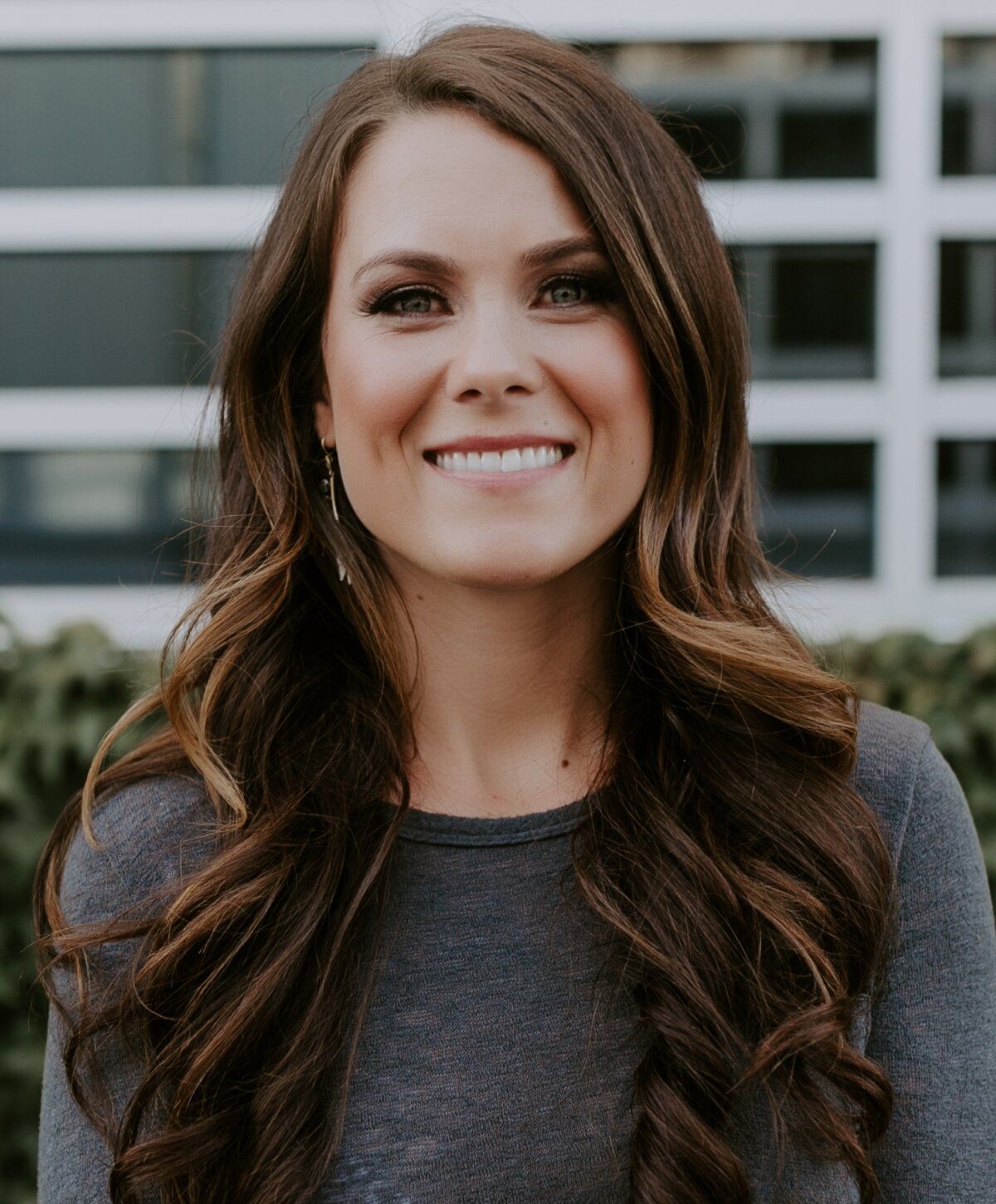 Smiling woman with wavy hair and grey shirt.