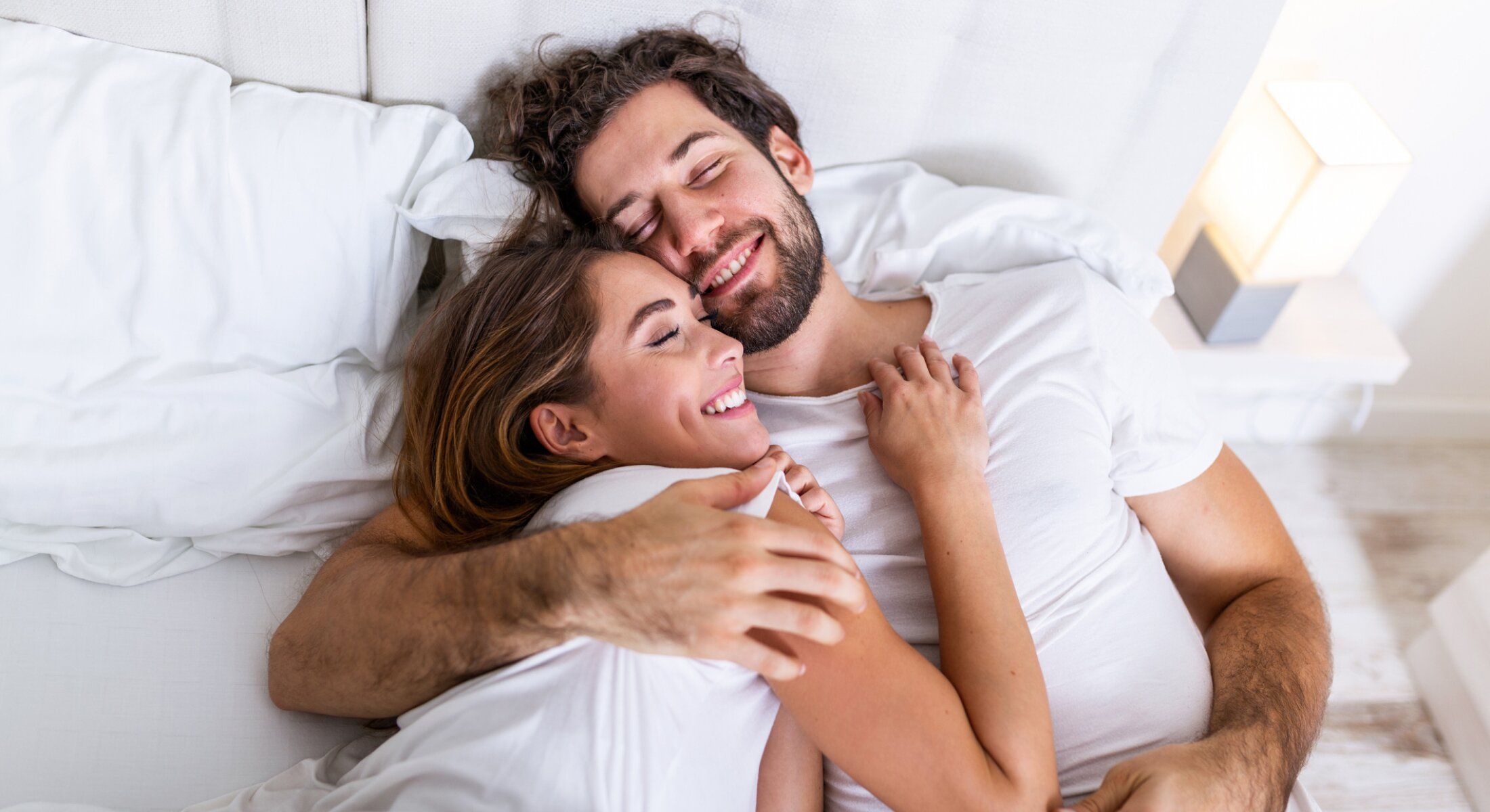 Couple cuddling happily on a bed.